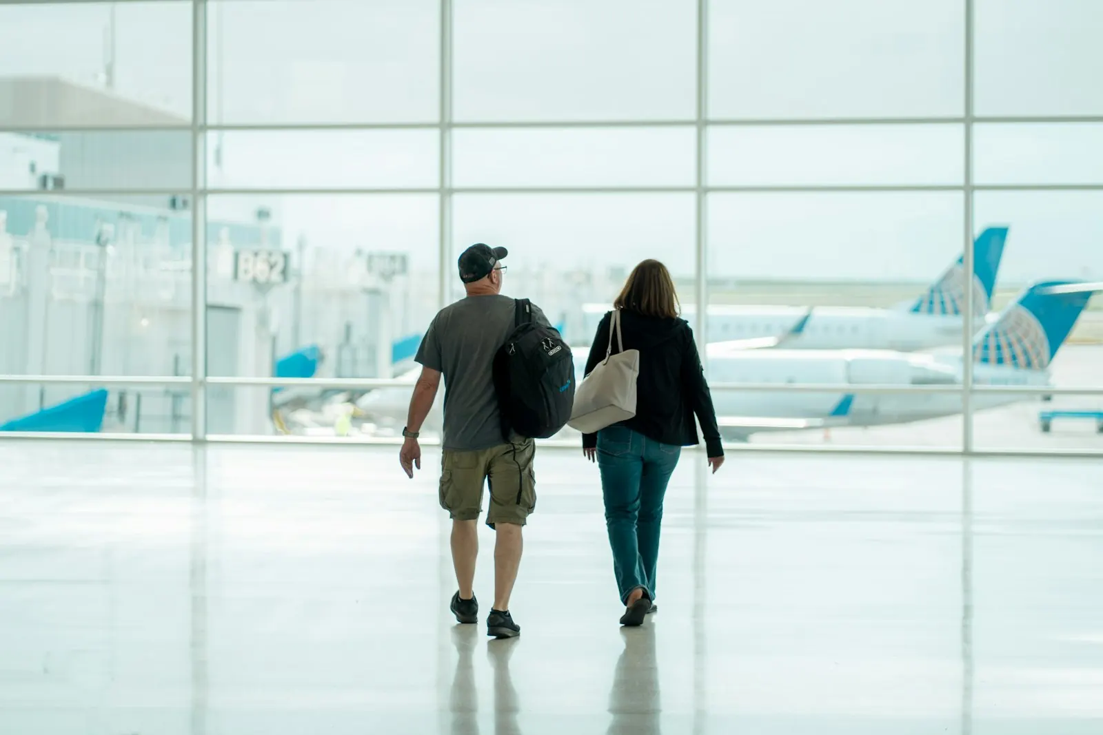 Casal caminhando no saguão de um aeroporto, com aviões ao fundo