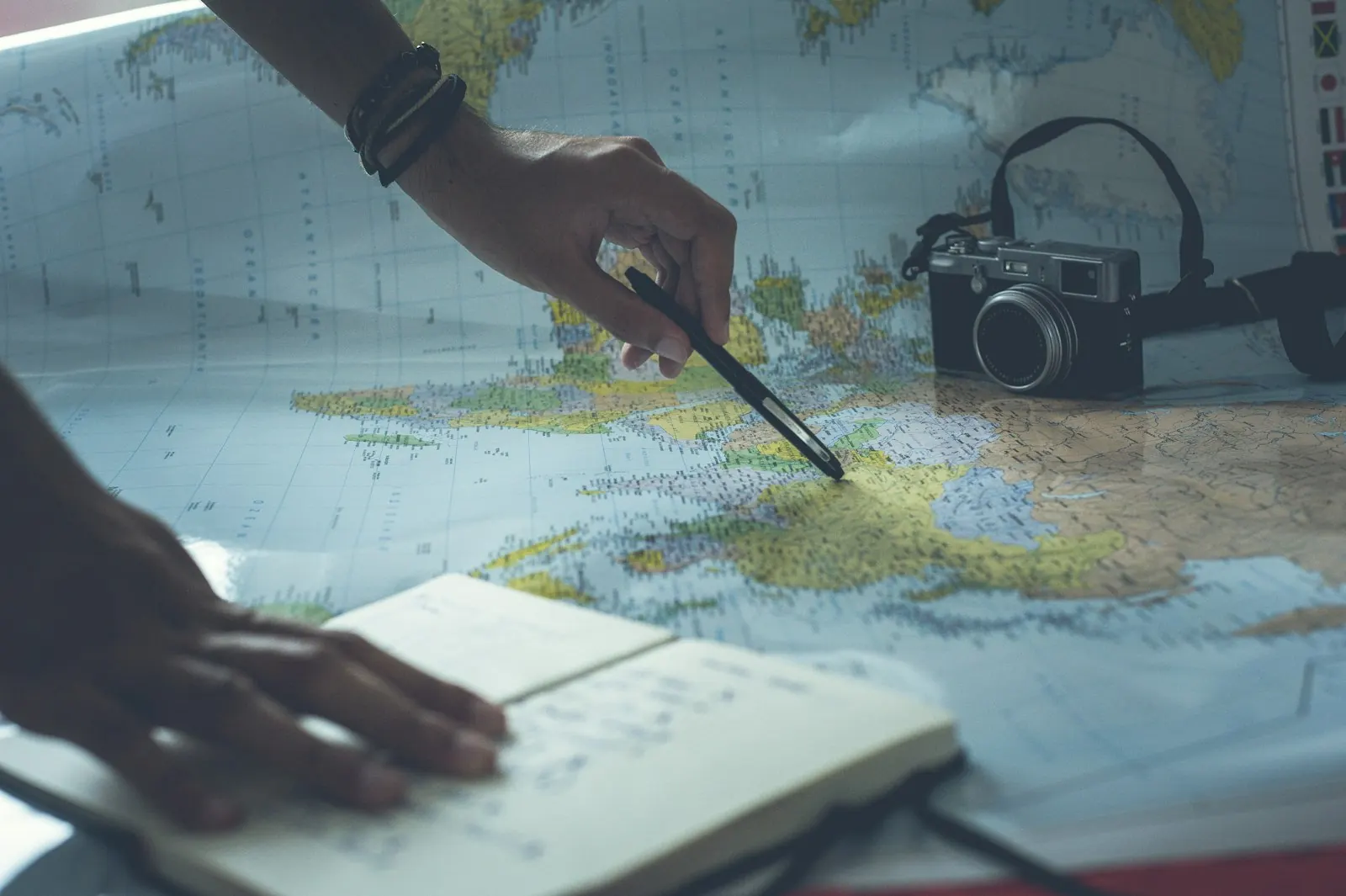 Pessoa planejando uma viagem com mapa, caderno e câmera sobre a mesa